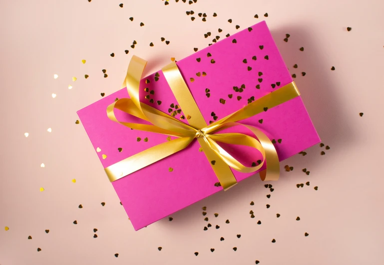 a pink and gold wrapped gift with shiny gold ribbons