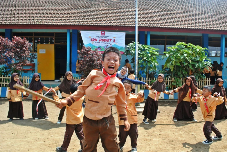 children in brown colored uniforms playing with some poles