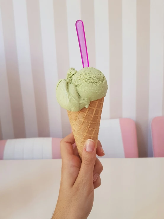 the hand holds an ice cream cone with a pink and blue straw in it