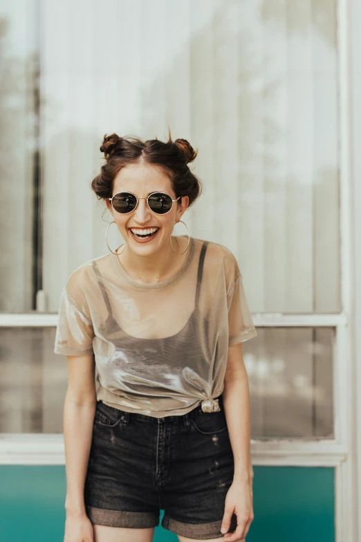 a smiling woman wearing a sheer t - shirt, black shorts, and sunglasses
