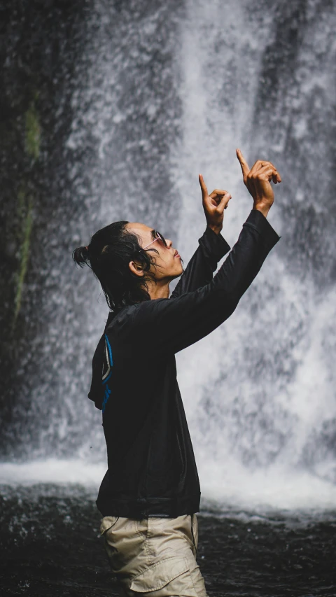 a man in a black shirt holding his hands in front of a waterfall