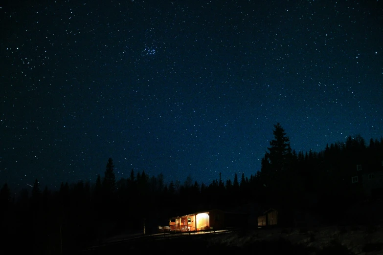 an illuminated cabin sits in the middle of the night