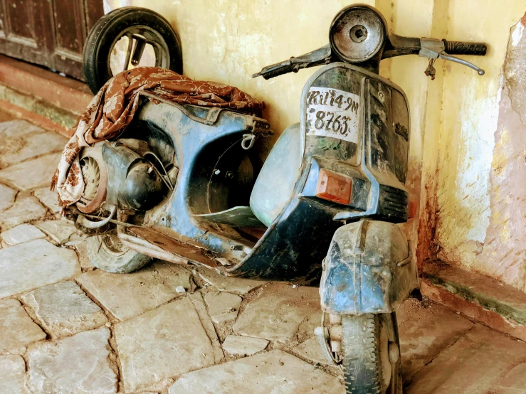 an old blue motor scooter is parked against a building
