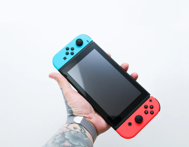 a person holds up a small blue and red nintendo wii game console