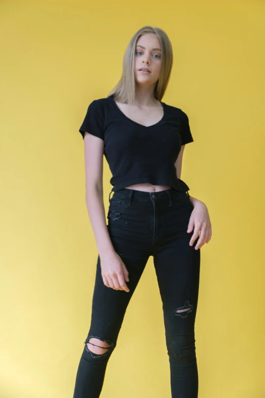 a young woman wearing ripped jeans poses in front of a yellow background