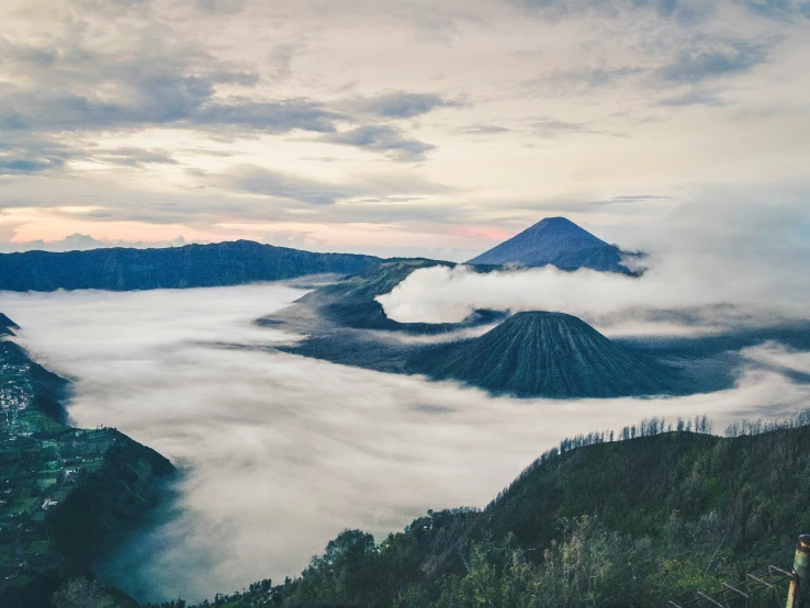 mountains and clouds are above the water and trees