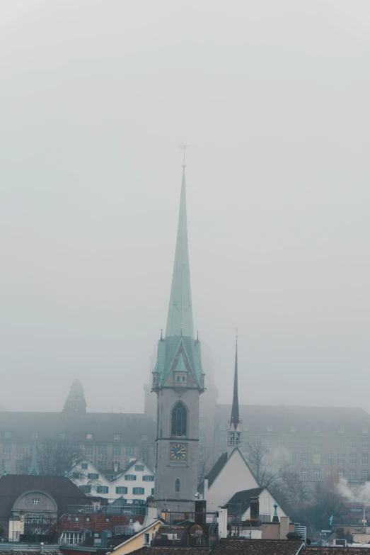 a church spire towering over a city on a foggy day