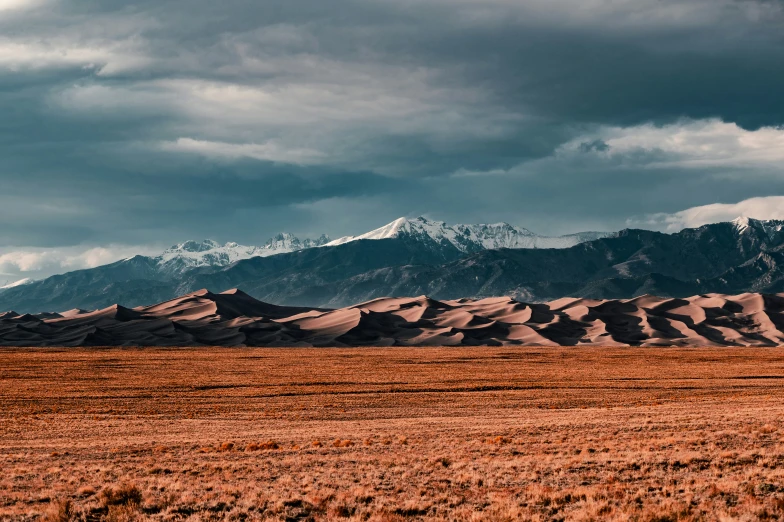 the mountains are in a line in front of some brown grass