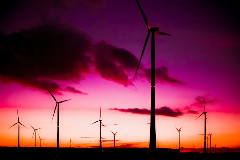 several wind mills at dusk with the setting sun behind them