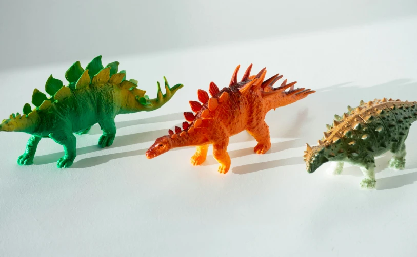 three toy dinosaurs stand together on the white surface
