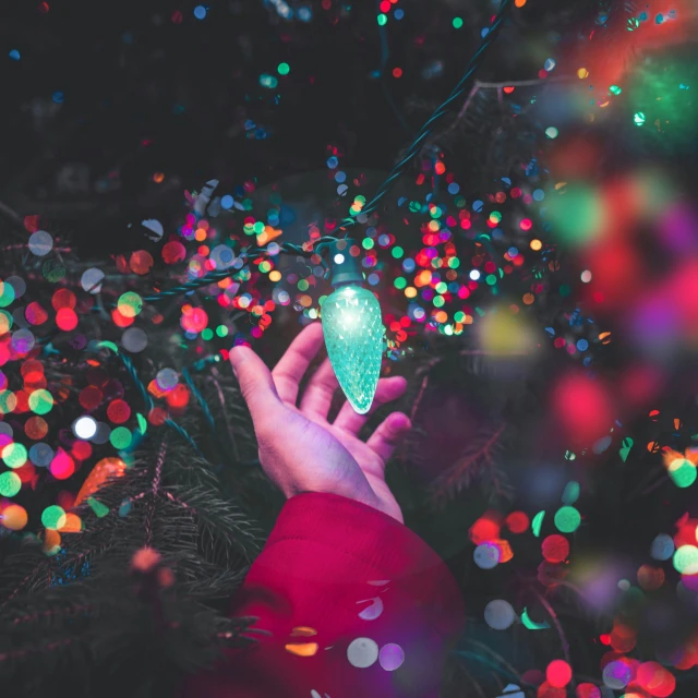 a hand holding a glowing christmas ornament in front of a blurry background
