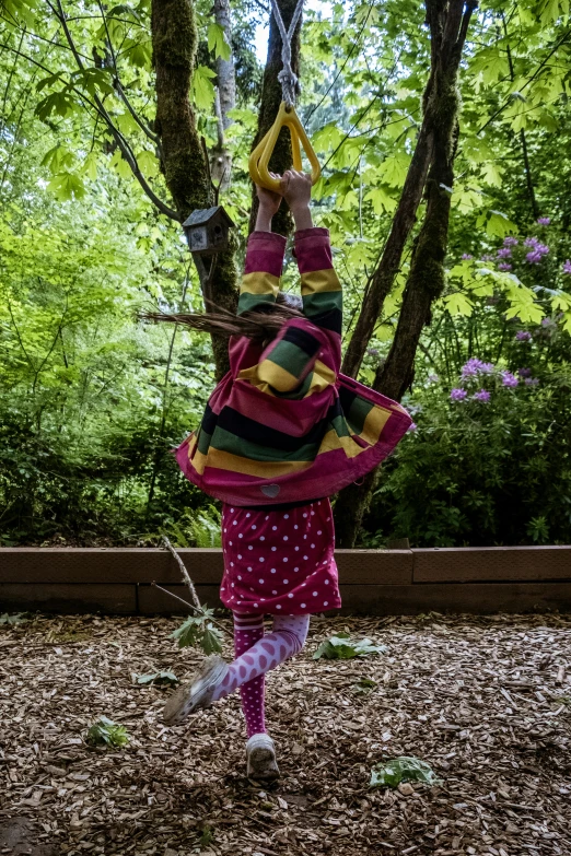 a  dressed in pink and yellow swings on a rope between two trees