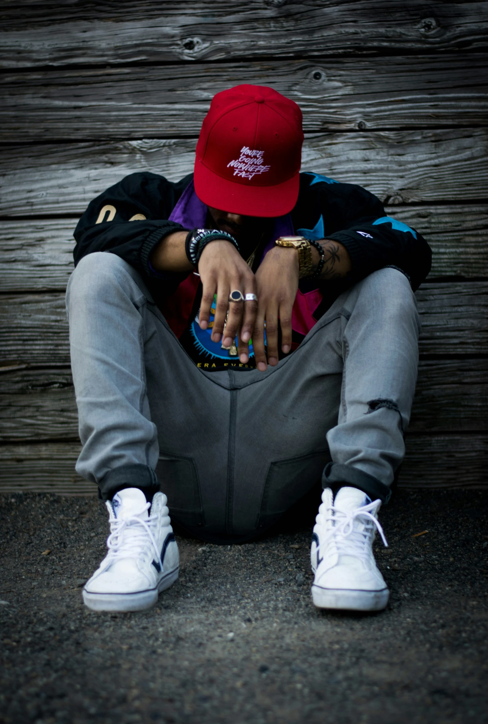 a person sitting in the shade of a wooden wall wearing white sneakers and a red hat