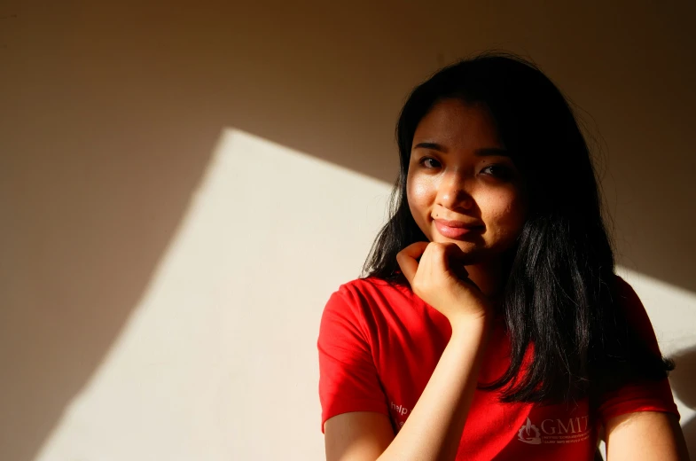 a woman in a red shirt leaning against a wall