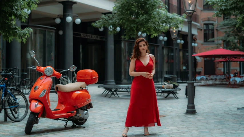 a woman in a red dress standing next to a moped