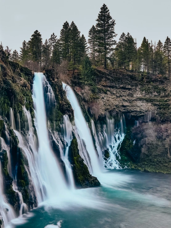 a large waterfall is near some trees in the woods