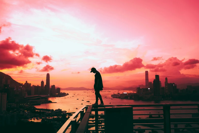 man stands on ledge while a sunset reflects off in the ocean