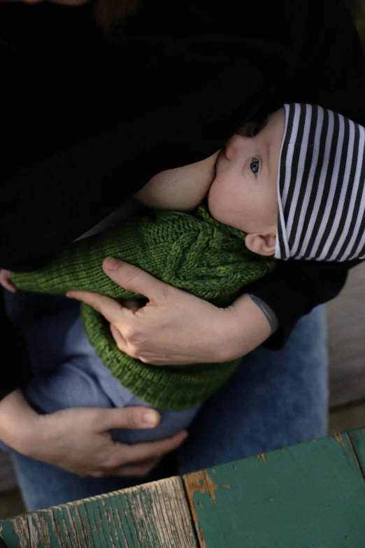 a baby wrapped in a sweater with a hat and holding a persons hand