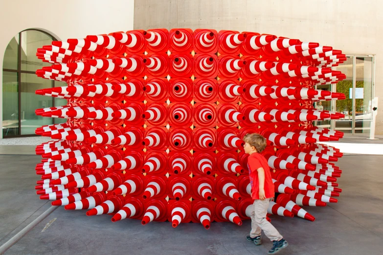 a child walks past a sculpture made with red and white circles