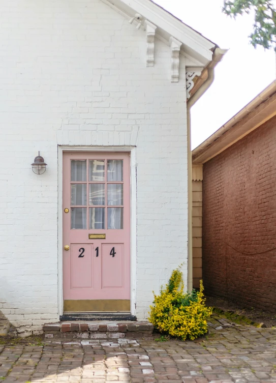 a white building with a pink door and brick driveway