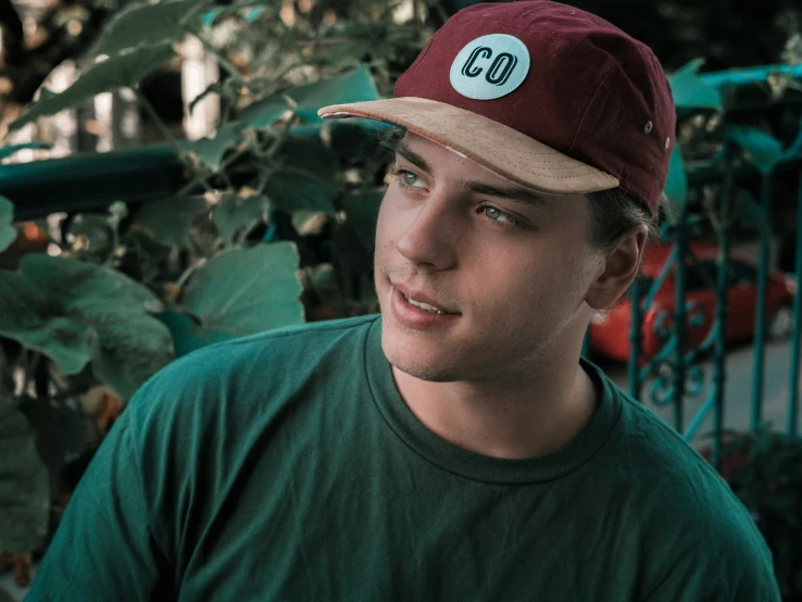 young man wearing green shirt and red cap standing outdoors