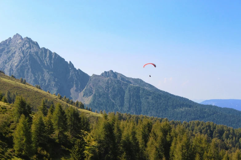 two people parasailing over mountains with pine trees