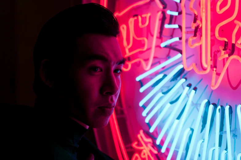 a young man standing next to a neon sign
