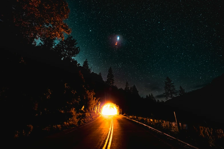 a car is driving on the road with lights on and stars above it