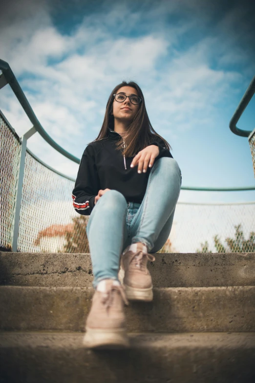 a woman wearing glasses sits on stairs in the sun