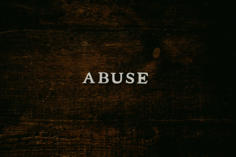 close up of the word abuse on top of a black wood background
