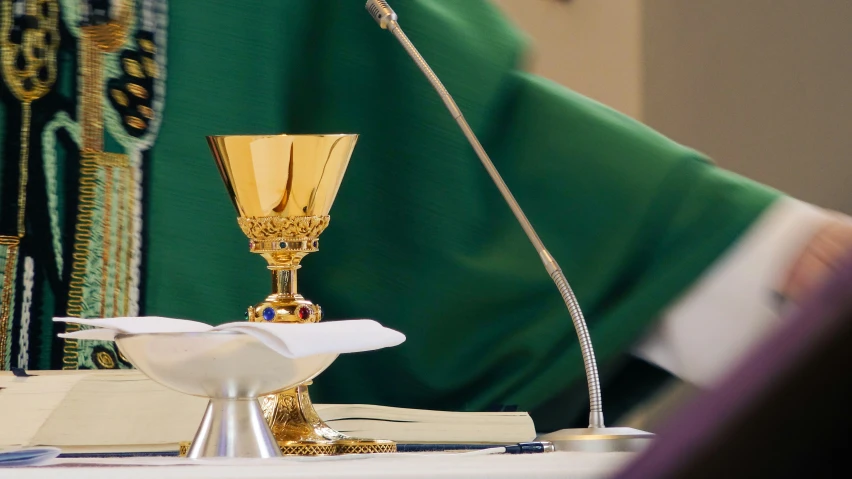 a priest is holding a holy book with a tall gold chalice