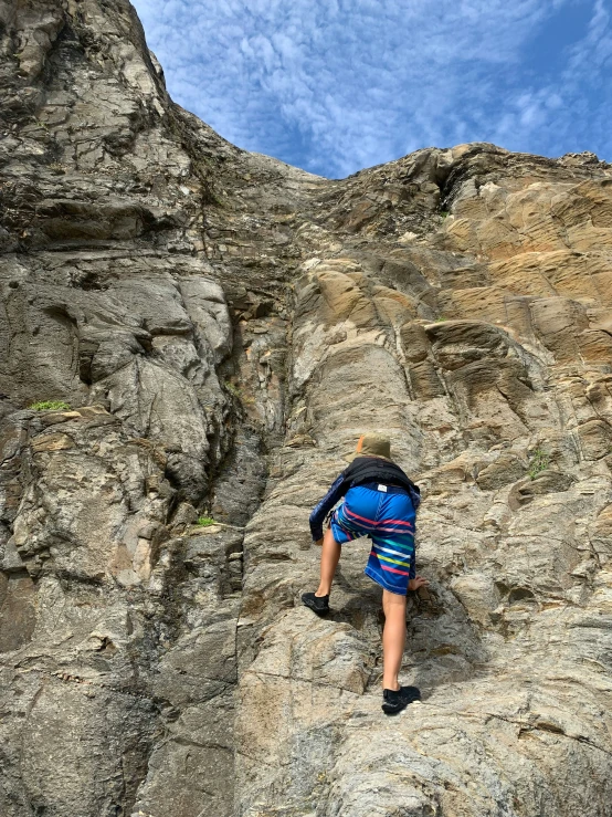 the man in the blue jacket climbing up a steep rock