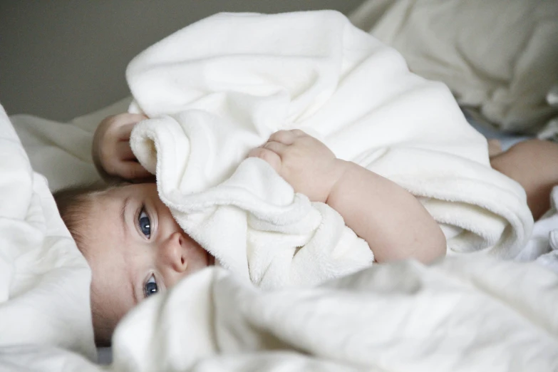 a baby laying under a blanket on top of a bed