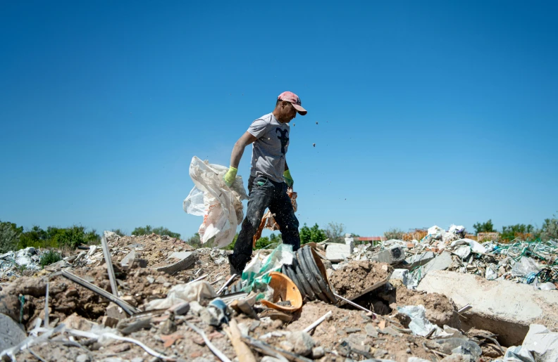 a man walking through a field with garbage