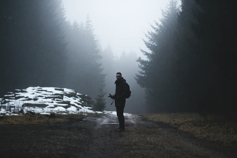 a man on a snow covered road in the middle of a forest