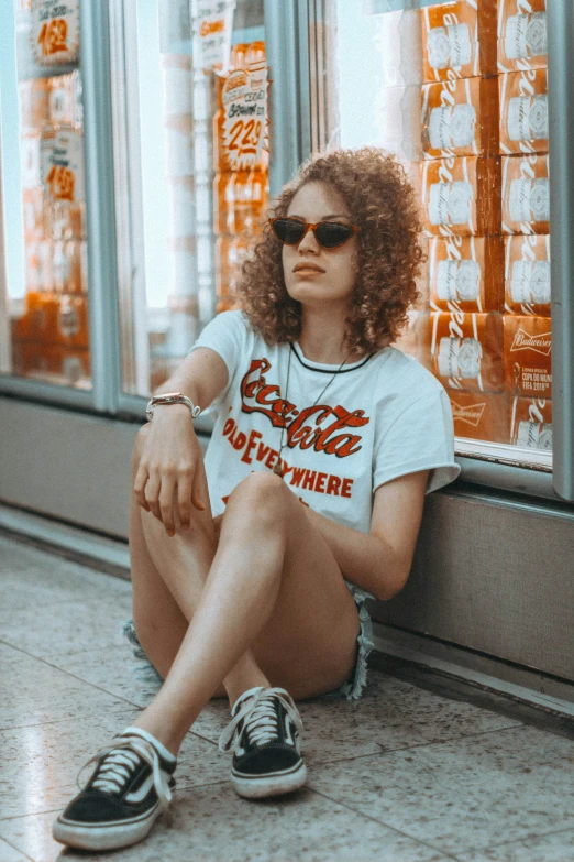 a young woman wearing sunglasses sitting on the ground