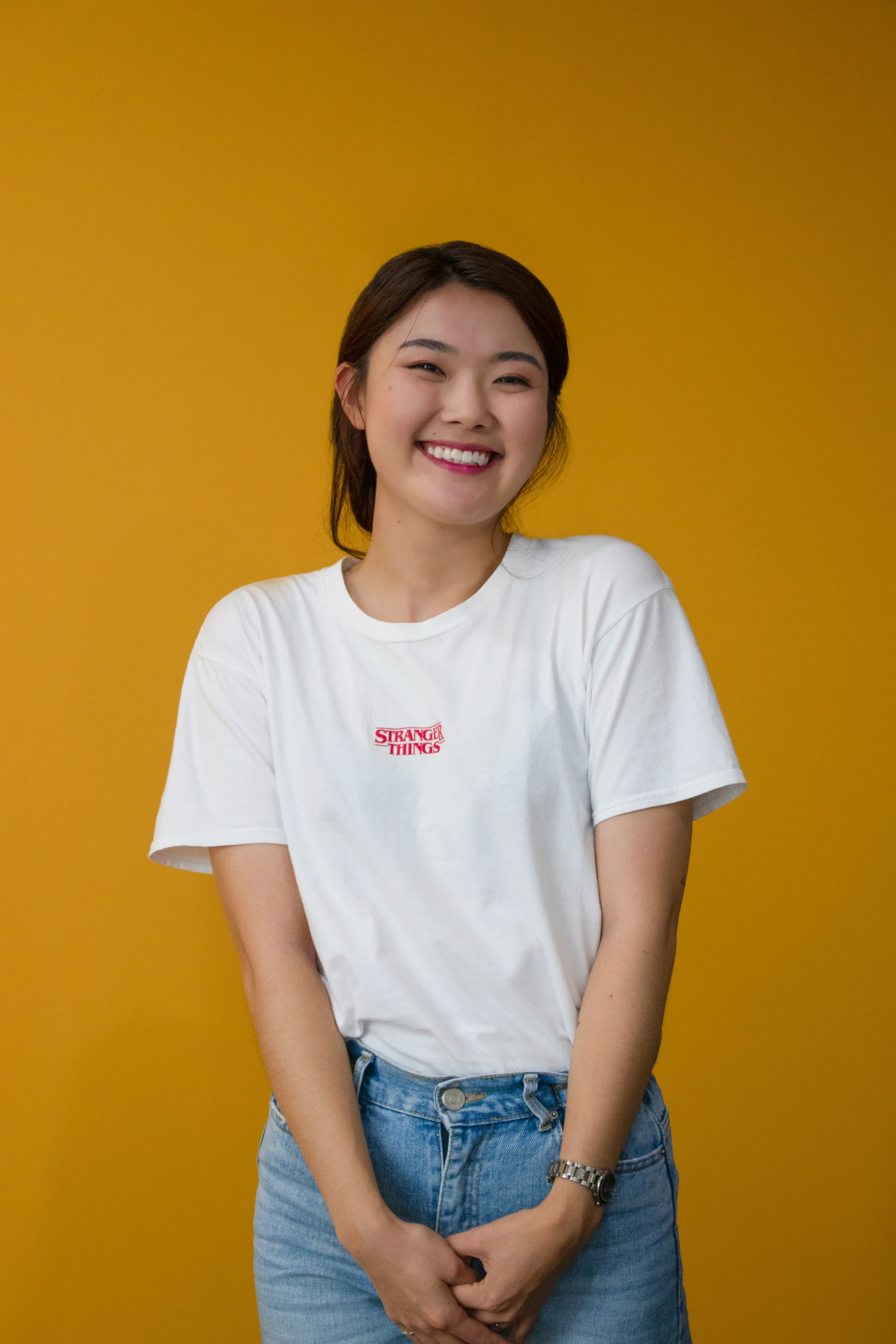 a young woman with long hair in shorts and a white shirt stands with her arms folded smiling