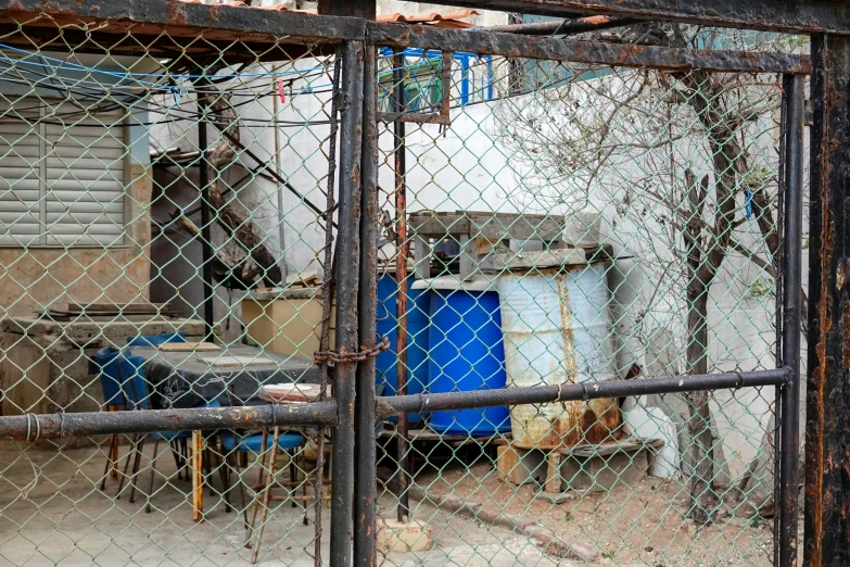 an open fence next to a building with a container and a blue barrel on it