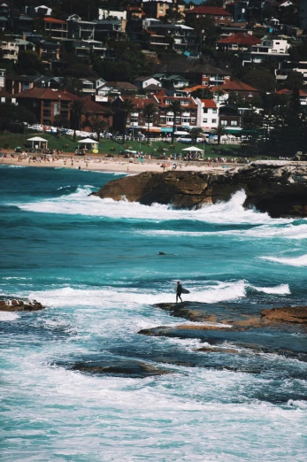 a person standing on a cliff by the water, holding his surfboard