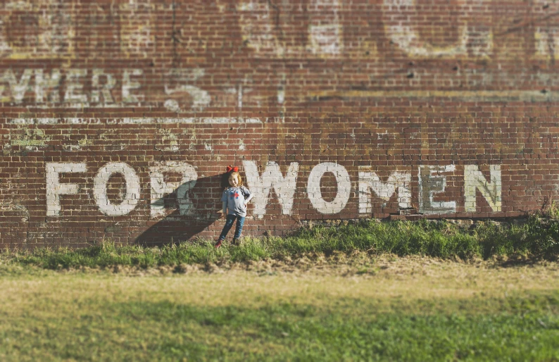 a woman walks past a faded building with writing