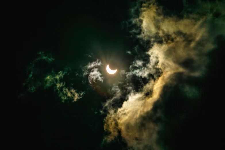 the moon is partially obscured by clouds and trees