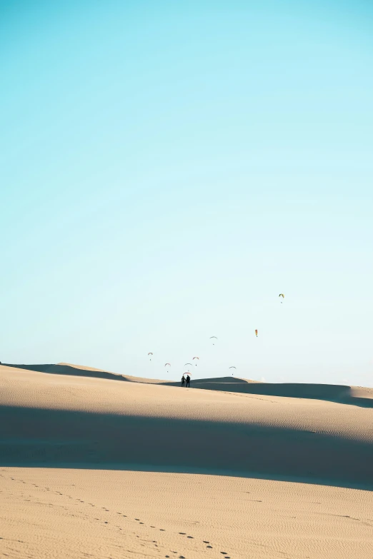 people in the desert walking toward several kites in the sky