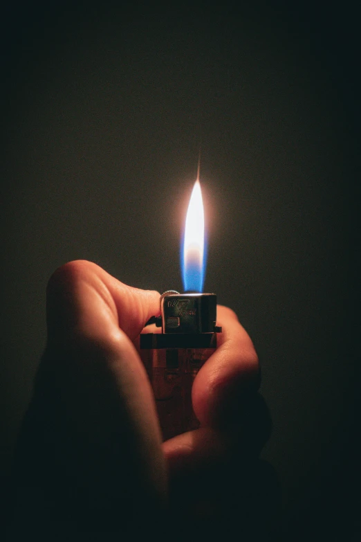 a hand holds an open matchbox lit by a candle