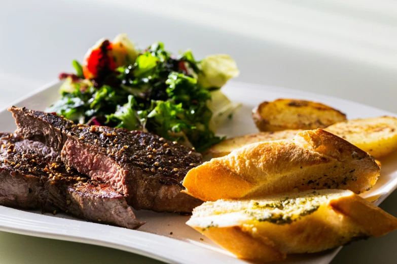 a white plate topped with steak and side dish of potato bread