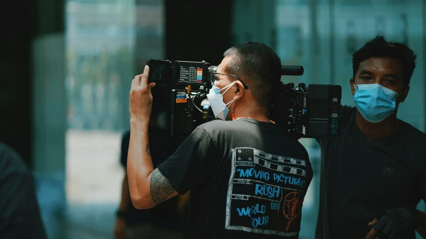 a man wearing a face mask with a cameraman recording