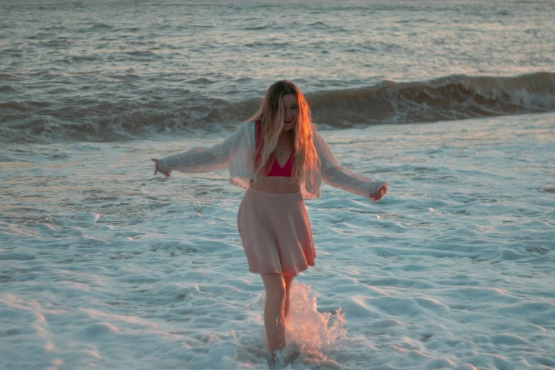 a girl in a dress standing in the water on a beach
