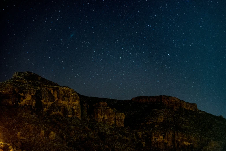 a large mountain with several trees on the side under night sky with stars