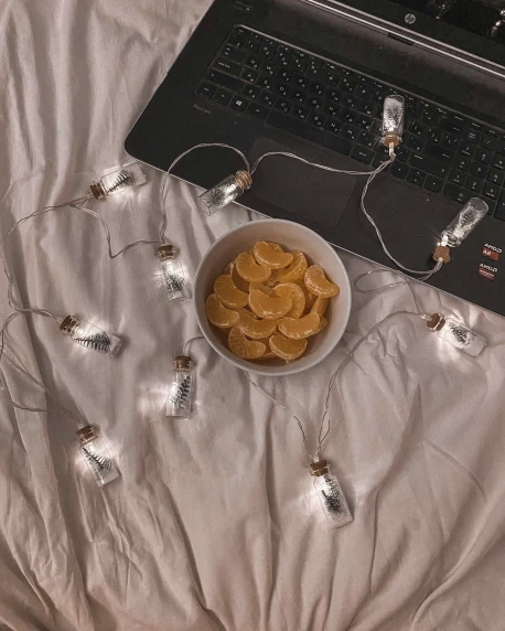 a bowl of small chips and a laptop on a bed
