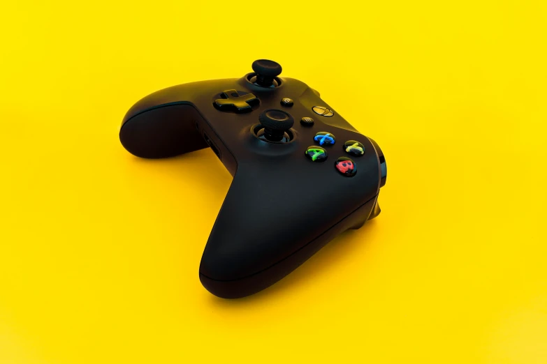 a black video game controller laying on top of a yellow surface