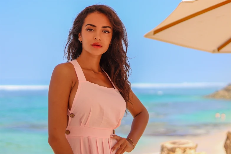 a woman with long hair standing on the beach wearing a pink dress